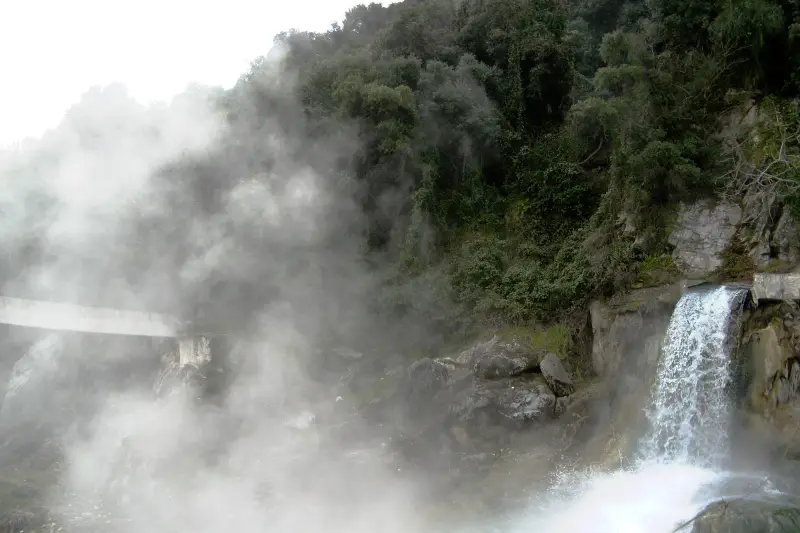 Steam rising off the thermal waterfall at Thermopylae's hot springs, tumbling over rocks beside a footbridge