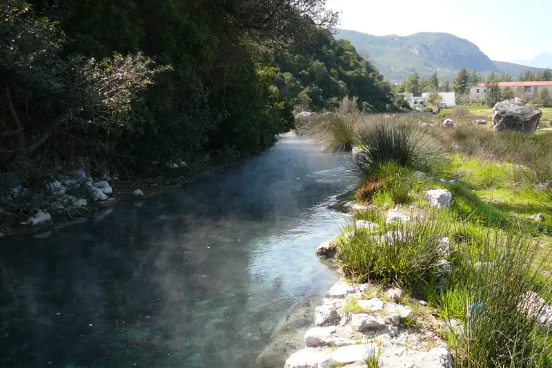 The turquoise thermal stream at Thermopylae's hot springs, lined with stone steps and reeds