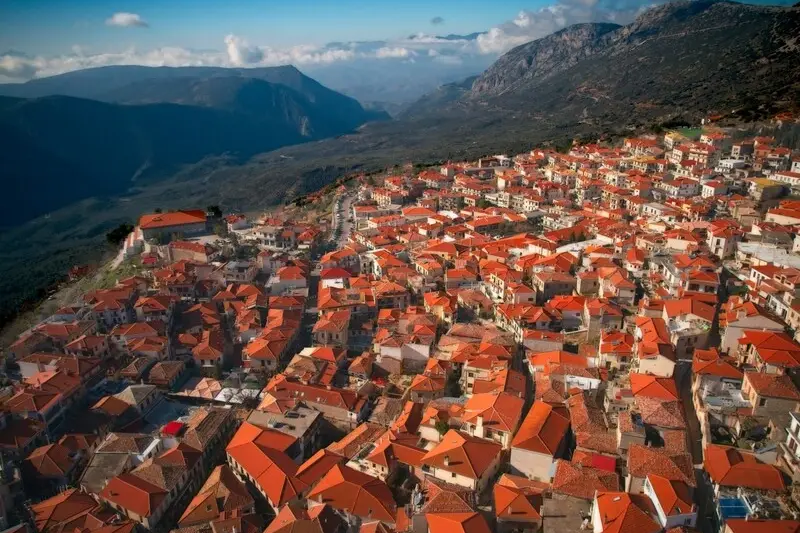 An aerial view of Arachova's red-tiled roofs spread across the mountainside at sunset
