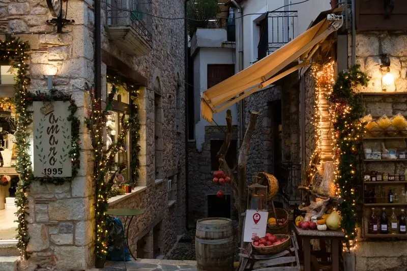 A stone-built shopfront in Arachova strung with fairy lights and hung with local produce at dusk
