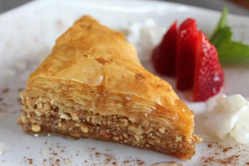 A slice of baklava dusted with cinnamon, served with fresh strawberries and cream