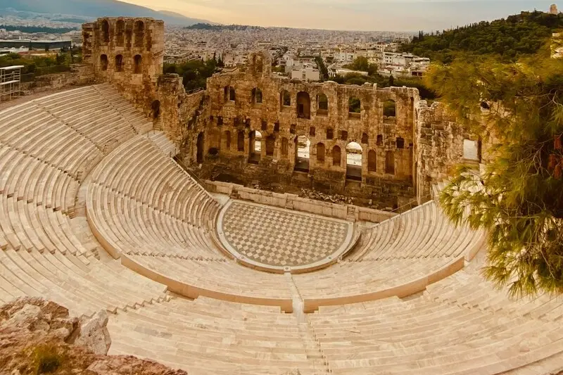 The Odeon of Herodes Atticus at sunset, its stone tiers and arches seen from above with Athens spread out behind it