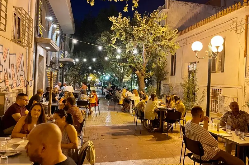 Diners at outdoor tables on a lantern-lit Athens side street at night
