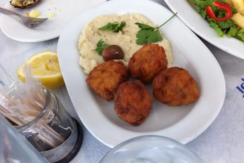 Four fried chickpea fritters (revithokeftedes) served with fava bean puree and an olive, a lemon half on the table beside the plate