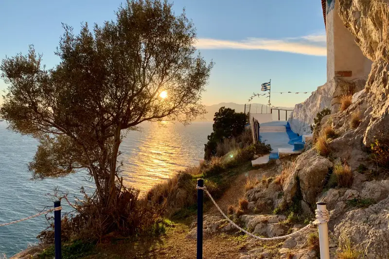An olive tree and a Greek flag on the Sounion coast as the sun sets over the sea