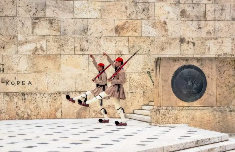 Two Evzones mid-stride in traditional uniform during the changing of the guard outside the Greek Parliament